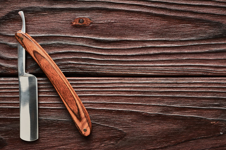 Straight razor partially open against two darkly stained wooden boards
