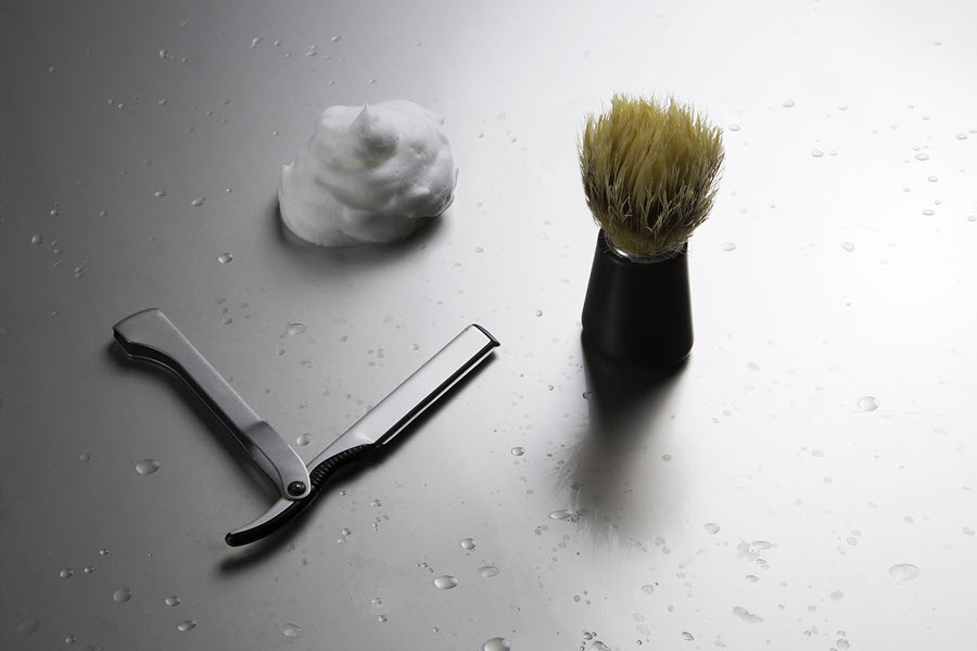 Image of a Dovo shavette, , shaving brush, and a dollop of shave cream on a surface wet with water droplets.